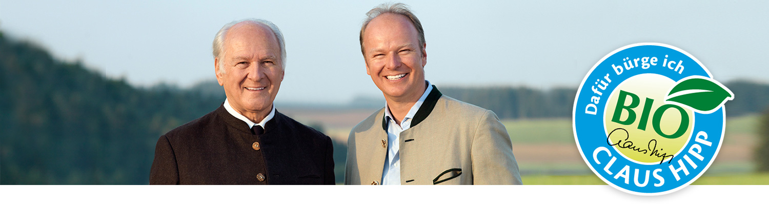 Two men in suits stand outdoors with a logo featuring a leaf and the word “BIO” in the foreground.