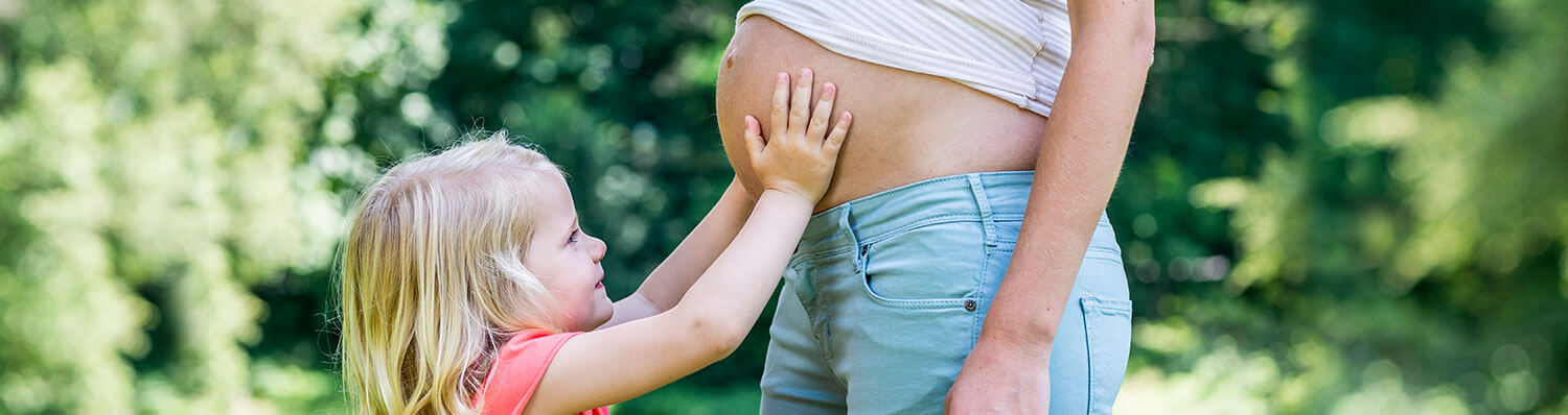 A child places their hand on the belly of an adult.
