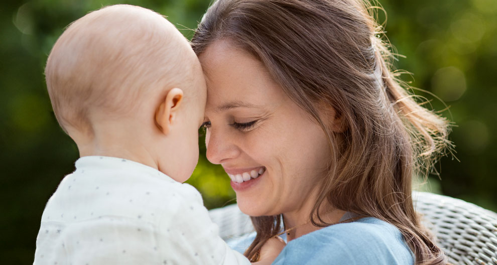 A woman and a baby share a moment of connection outdoors.