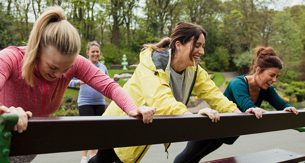 Four women are outdoors, engaging in physical activity on a bench.