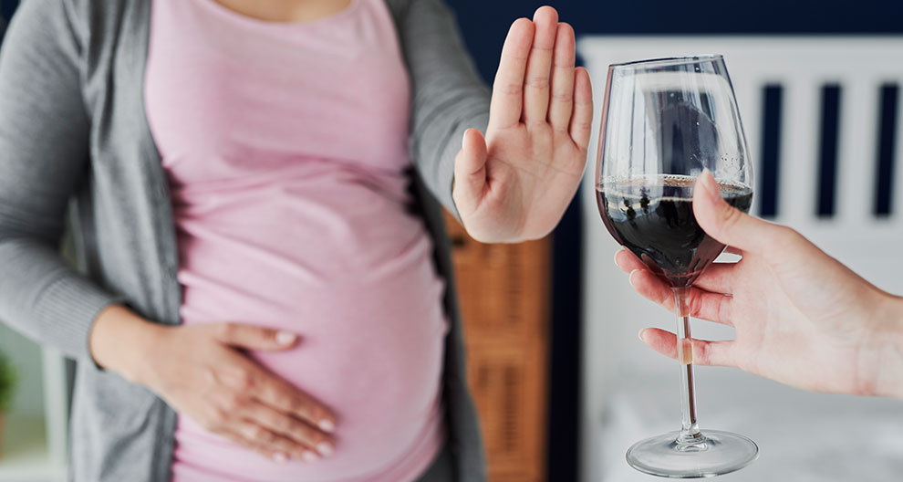 A pregnant woman refuses a glass of red wine.