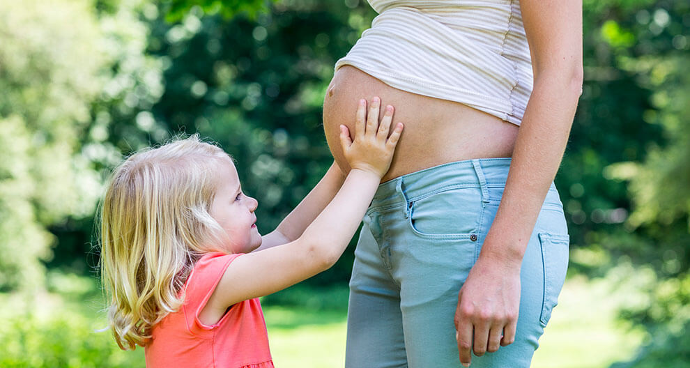 A child in a pink shirt places her hand on a pregnant woman's belly.
