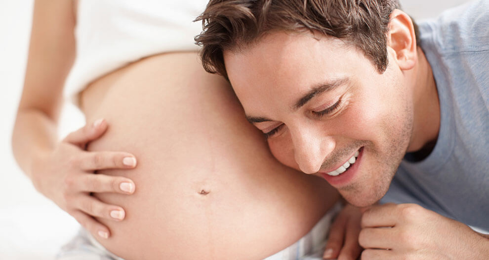 A man lovingly embraces a pregnant woman.